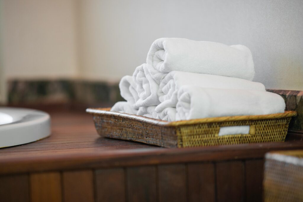 Basket of freshly folded white towels placed on a wooden surface, emphasizing cleanliness and comfort.