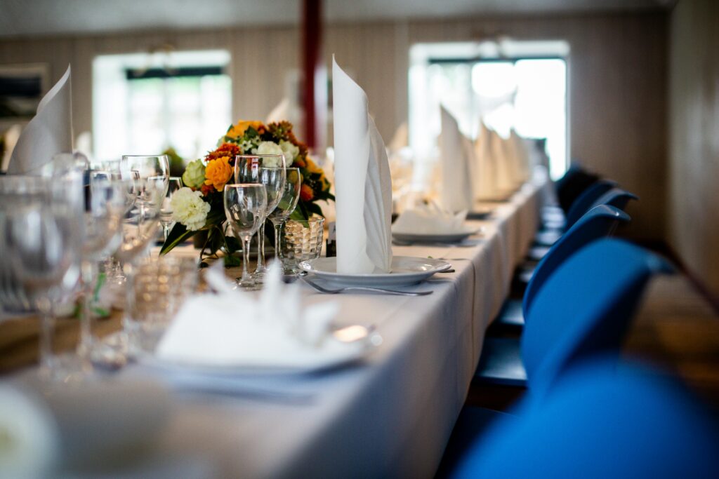 Elegant indoor dining table with white napkins, glassware, and a floral centerpiece, set in a softly lit room with blue chairs.