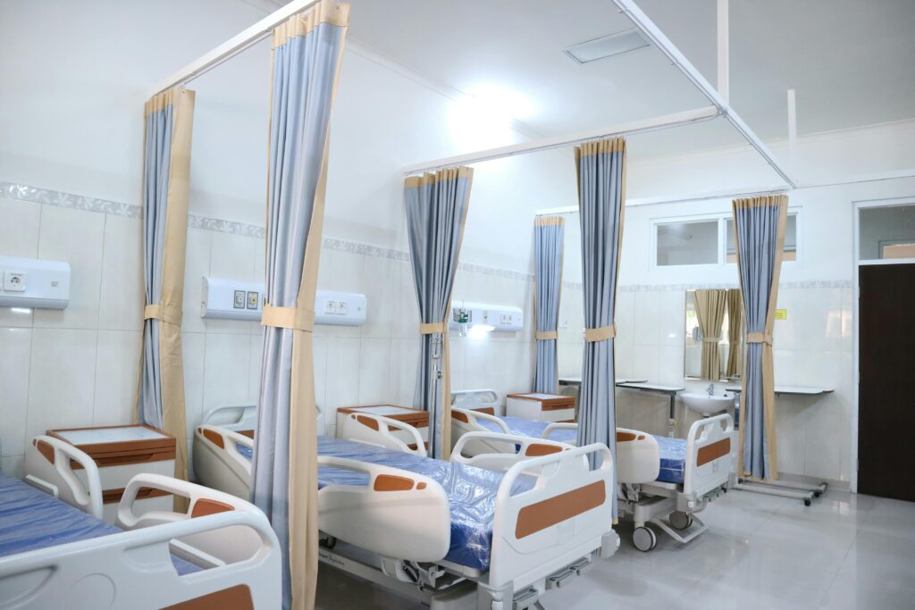 Hospital room with neatly arranged beds, privacy curtains, and essential medical equipment for patient care.