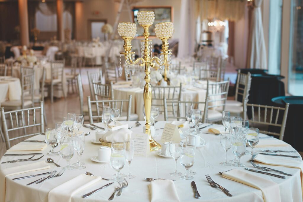 Elegant banquet table with white linens, silver chairs, and a gold candelabra centerpiece, set for a formal event.